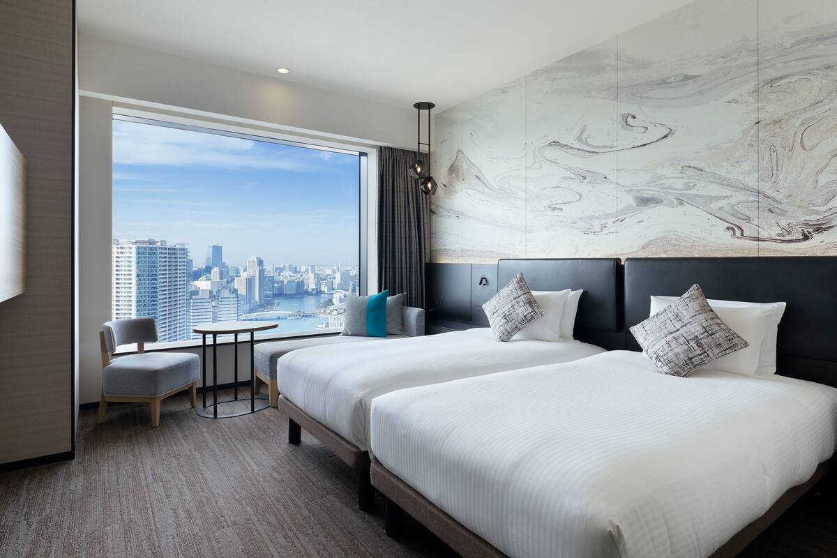 Habitación de hotel con dos camas, vistas a la ciudad, una mesita y una silla.