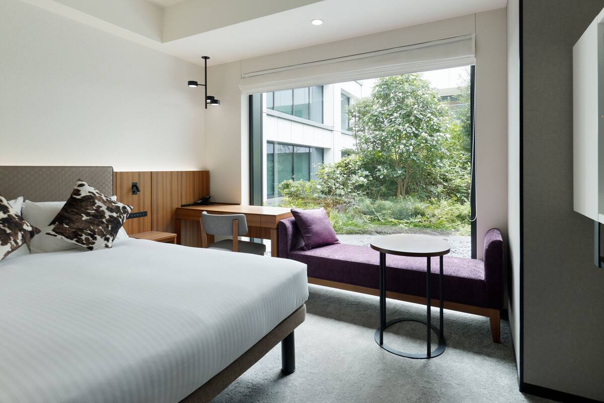 Una habitación de hotel con cama, escritorio, silla, una mesita pequeña y sofá.