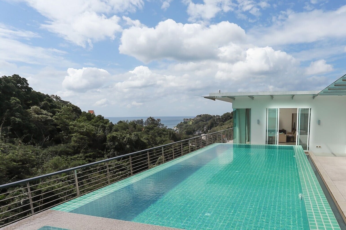 A modern house with a large swimming pool, a glass balcony, and a view of the sea.