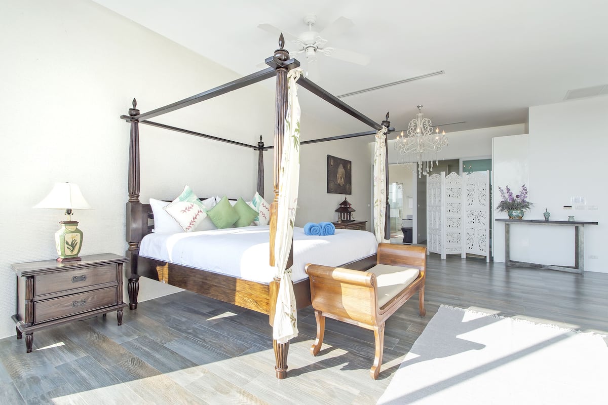 A four-poster bed with a canopy, a wooden nightstand with drawers, a bedside table with a lamp, and a wooden chair.