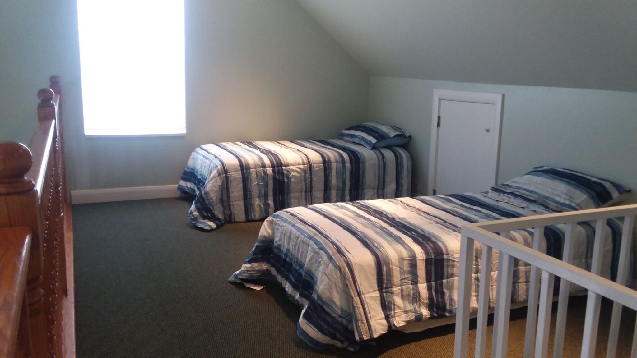 Une chambre avec deux lits, un berceau en bois, une fenêtre et une porte.