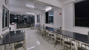A spacious dining area with long tables and chairs, large windows, and a modern ceiling design. - Collection O 49874 Plaza Inn (Guwahati)
