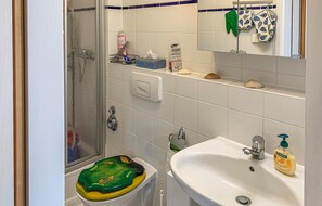 Ein Badezimmer mit Toilette, Waschbecken und Dusche. Auf dem Waschbecken stehen Pflegeprodukte und über dem Spiegel ist ein Handtuchhalter.