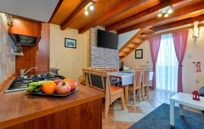 A kitchen with a wooden island, a dining area with a table and chairs, a stone wall, and a TV mounted on the wall. - Gorgeous home in Novi Marof with sauna (Novi Marof)