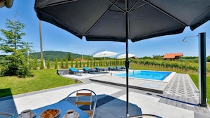 Ein Poolbereich mit Liegestühlen, einem Tisch mit Speisen und Getränken sowie Blick auf Weinberge und Hügel.