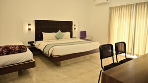 A hotel room with a large bed, a smaller bed, a desk, two chairs, a wall-mounted air conditioner, and a window with curtains. - Ags Holiday Resorts (Tirupattur)