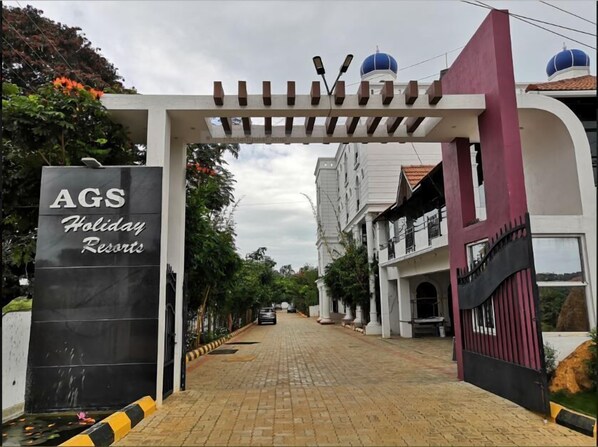 A gated entrance to AGS Holiday Resorts with a paved driveway leading to the buildings. - Ags Holiday Resorts (Tirupattur)