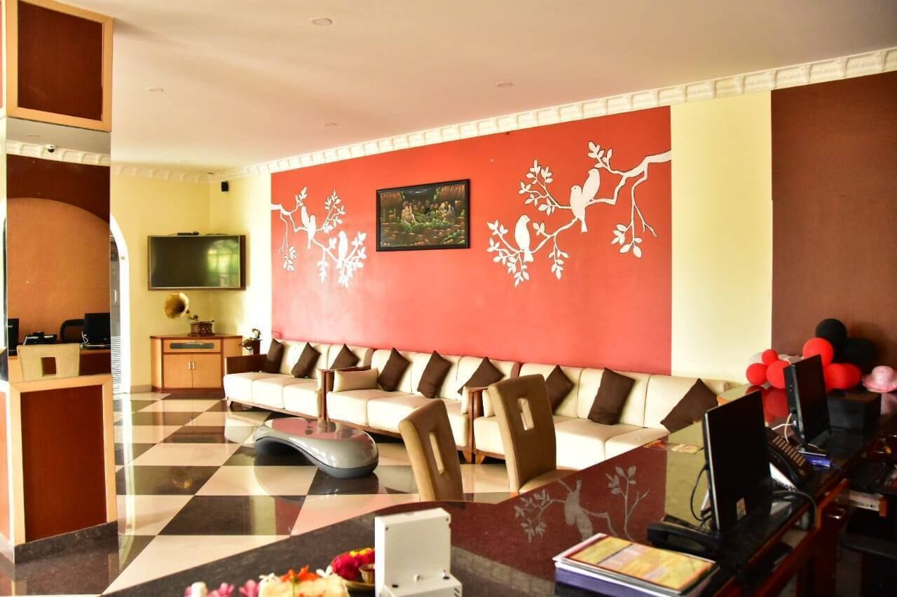 Een hotel lobby met een geruite vloer, een bank met bruine kussens, een televisie, en een muur versierd met afbeeldingen van vogels en bomen.