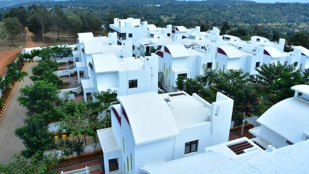 A cluster of white buildings with flat roofs, surrounded by greenery and a hilly landscape in the background. - Ags Holiday Resorts (Tirupattur)