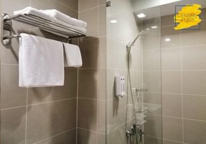 Uma casa de banho moderna com cabine de duche em vidro, um porta-toalhas com duas toalhas brancas e um dispensador de sabonete na parede.