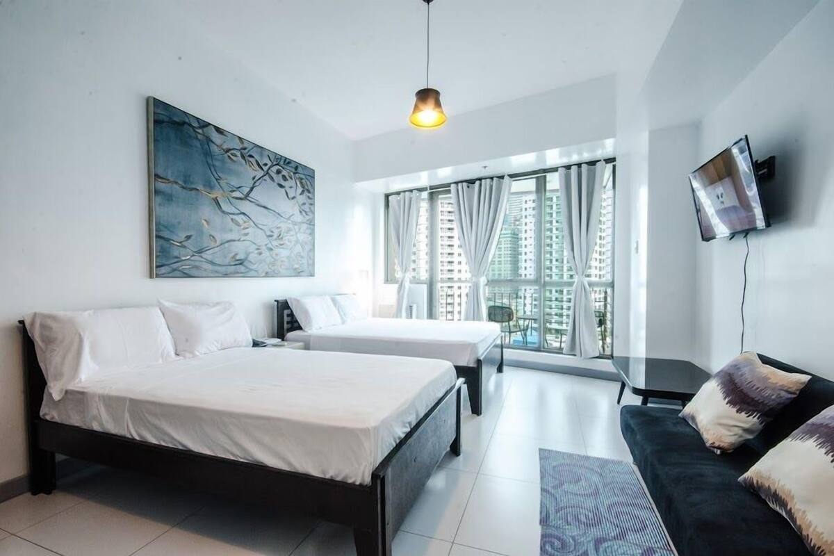 A modern hotel room with two beds, a sofa, a TV, and a large window with curtains.