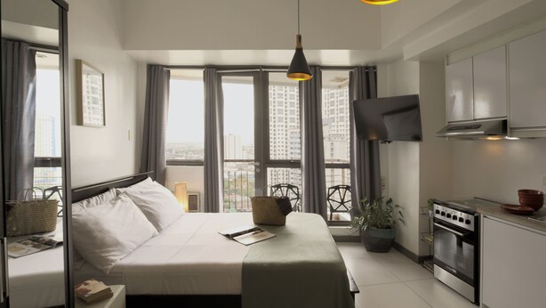 A modern hotel room with a large bed, a kitchen with a stove, and a TV mounted on the wall. - KL Tower - PH Staycation (Makati)