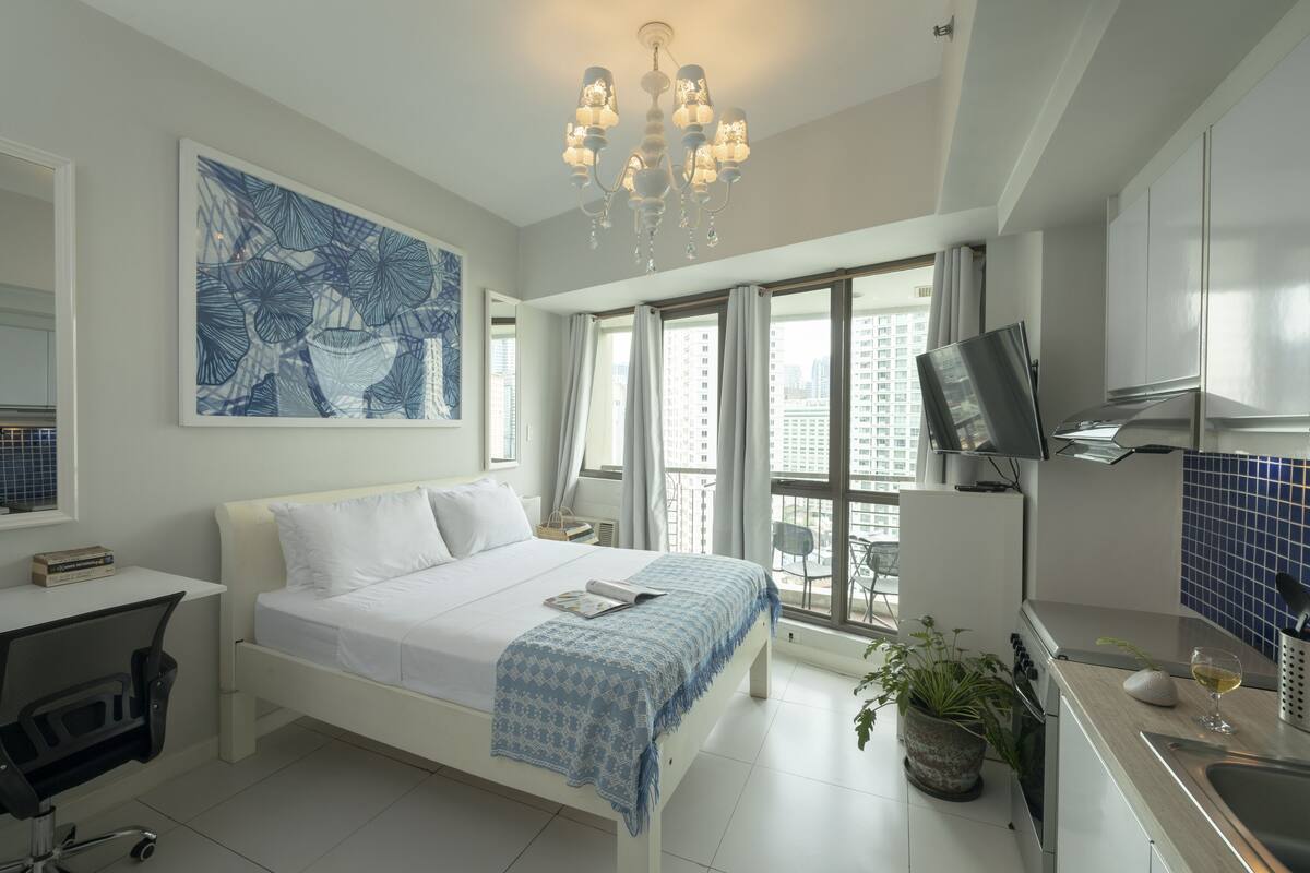 A modern hotel room with a large bed, a desk, a TV, and a balcony with a city view.