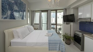 A hotel room with a bed, a TV, a kitchenette, and a balcony with a view of the city. - KL Tower - PH Staycation (Makati)