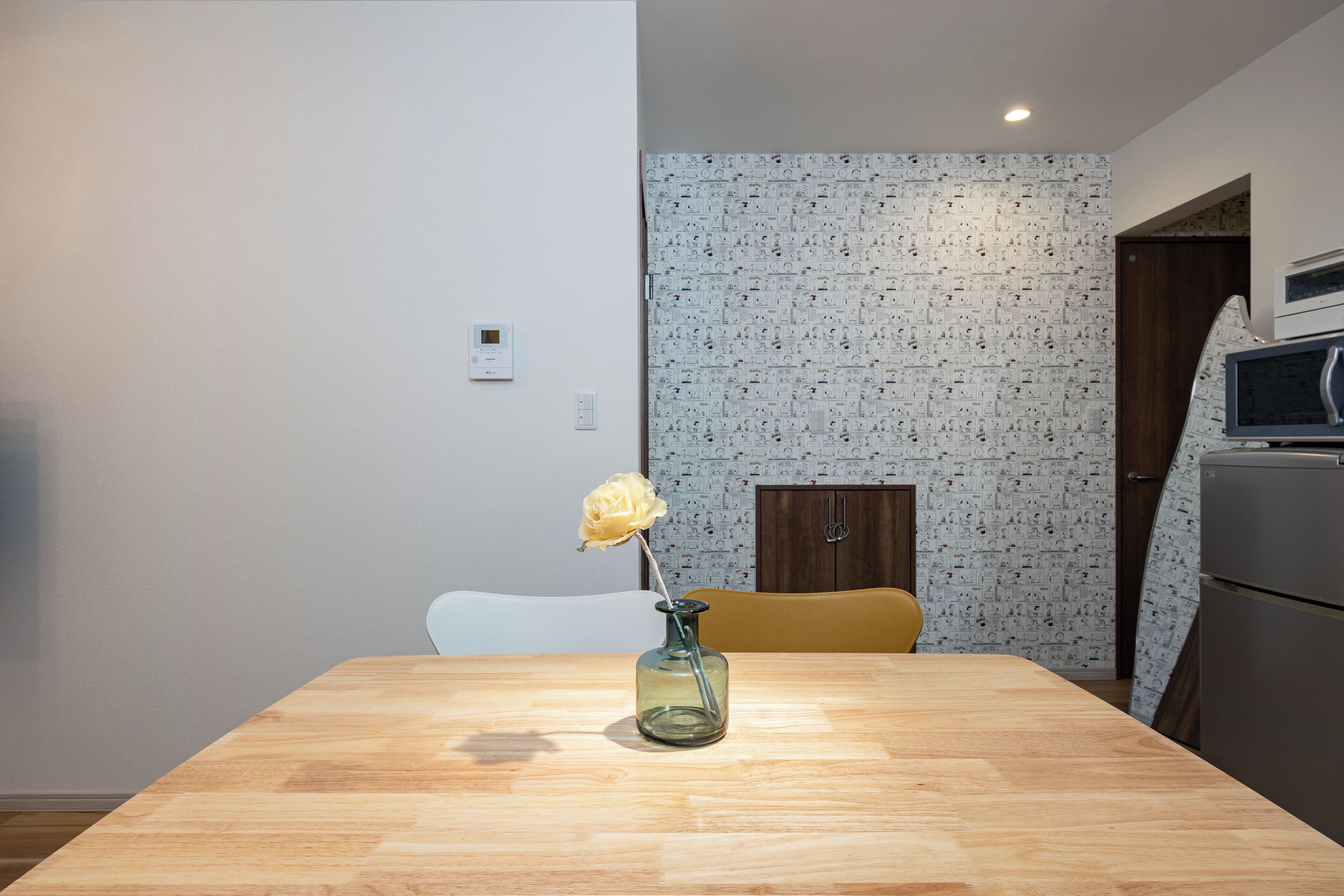 Une table à manger avec un vase contenant une seule fleur, une chaise blanche et un four à micro-ondes en arrière-plan.
