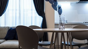 A modern living room with a round dining table, two chairs, a sofa with a blue pillow, and a kitchen in the background.