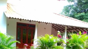 A house with a tiled roof, a red door, and a garden with various plants and a lawn.