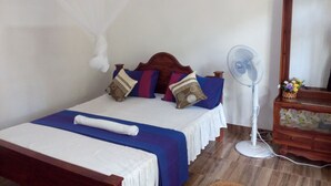 A bed with a mosquito net, a bedside fan, and a wooden dresser with a mirror.