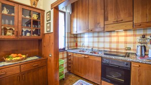 A kitchen with wooden cabinets, a granite countertop, a sink, a stove, and a window with a lace curtain.