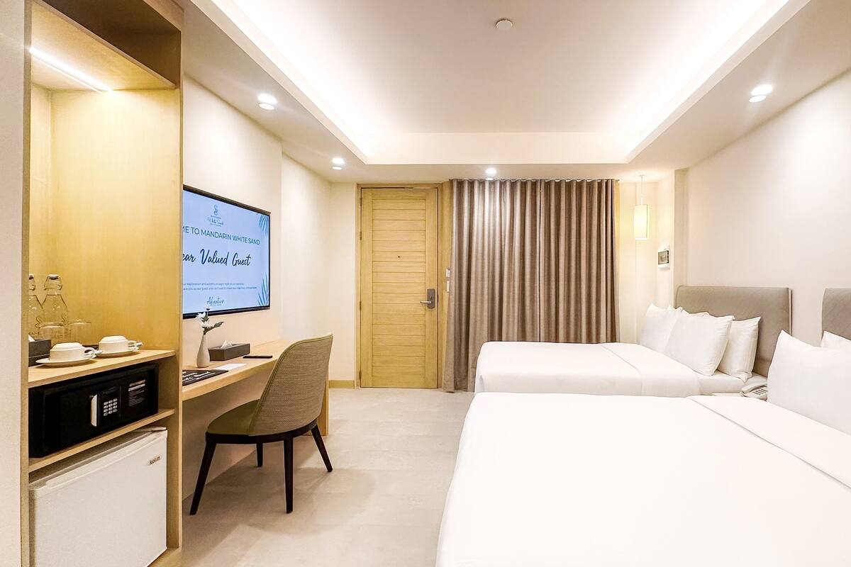 Una habitación de hotel con cama, escritorio con computadora, televisor y minibar.