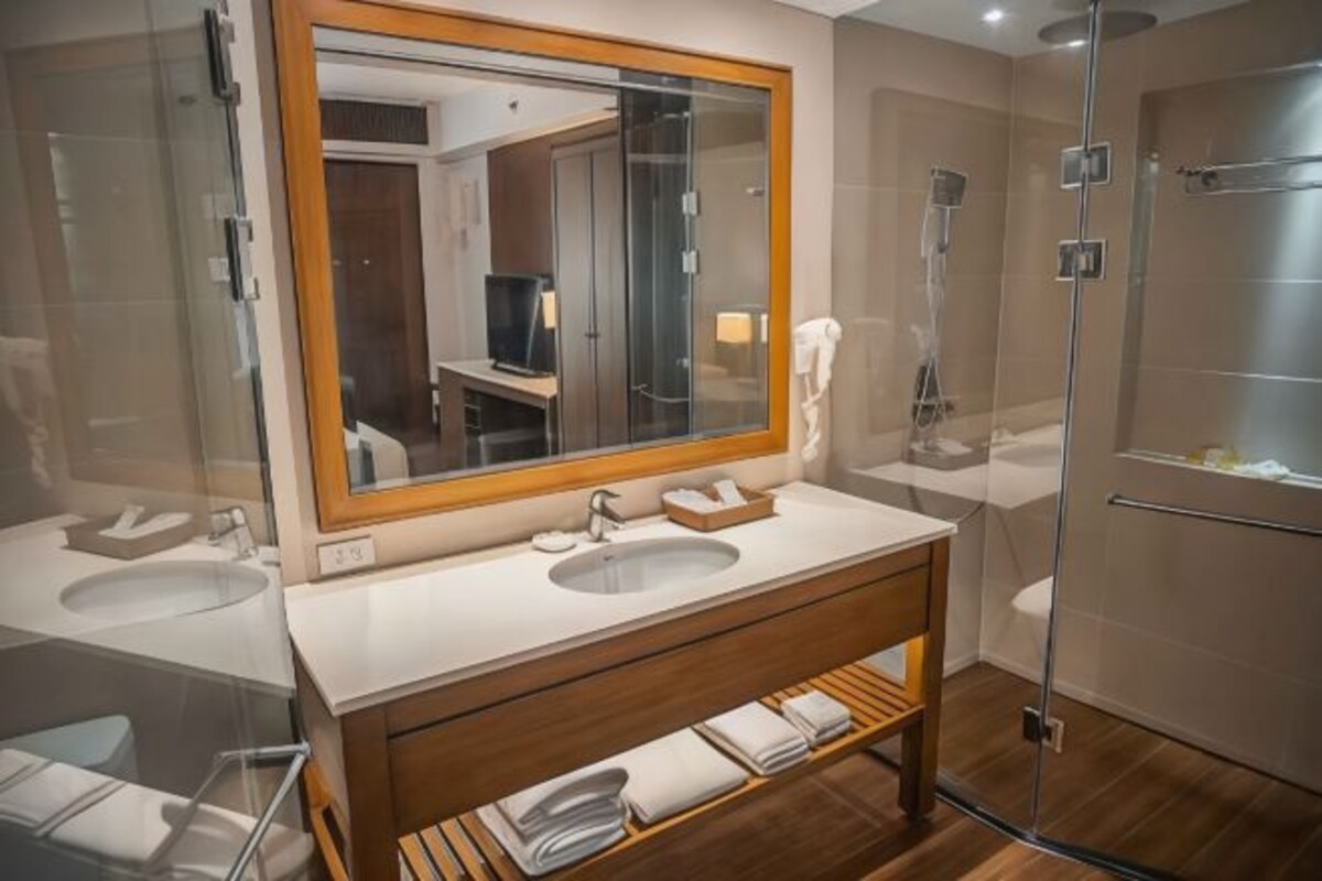 Un baño moderno con dos lavamanos, un espejo grande, un mueble de tocador de madera y una zona de ducha con mampara de cristal.