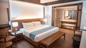 A hotel room with a large bed, wooden furniture, a bench, a nightstand, a lamp, a mirror, and a bathroom with a vanity and shower. - Mandarin White Sand Boracay (Boracay Island)