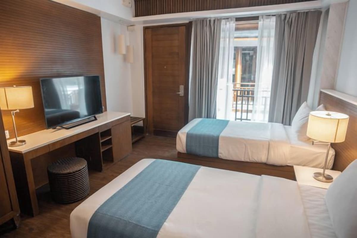 A hotel room with a TV, two beds, a desk, and a window with curtains.