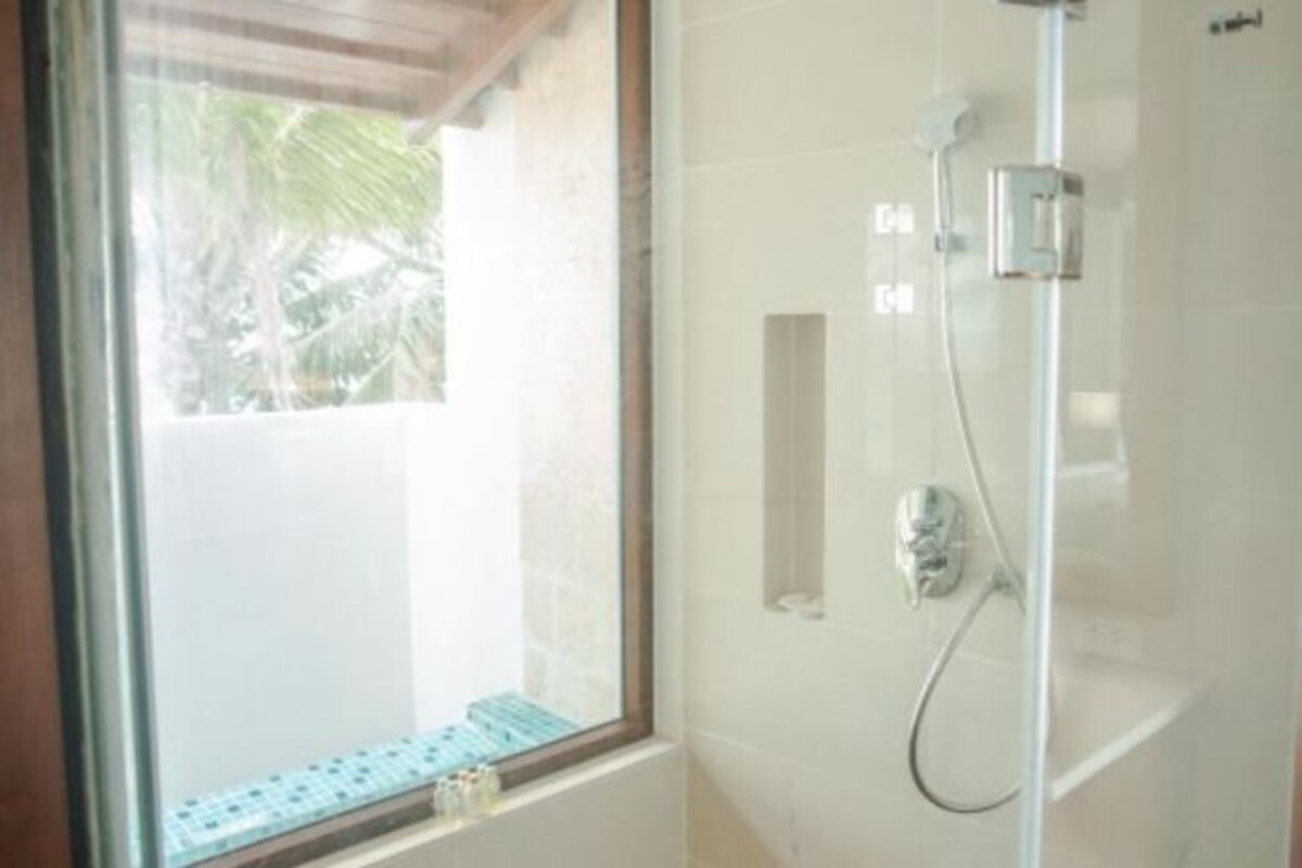 Zona de ducha con mampara de vidrio, ventana visible, pared con azulejos y ducha.
