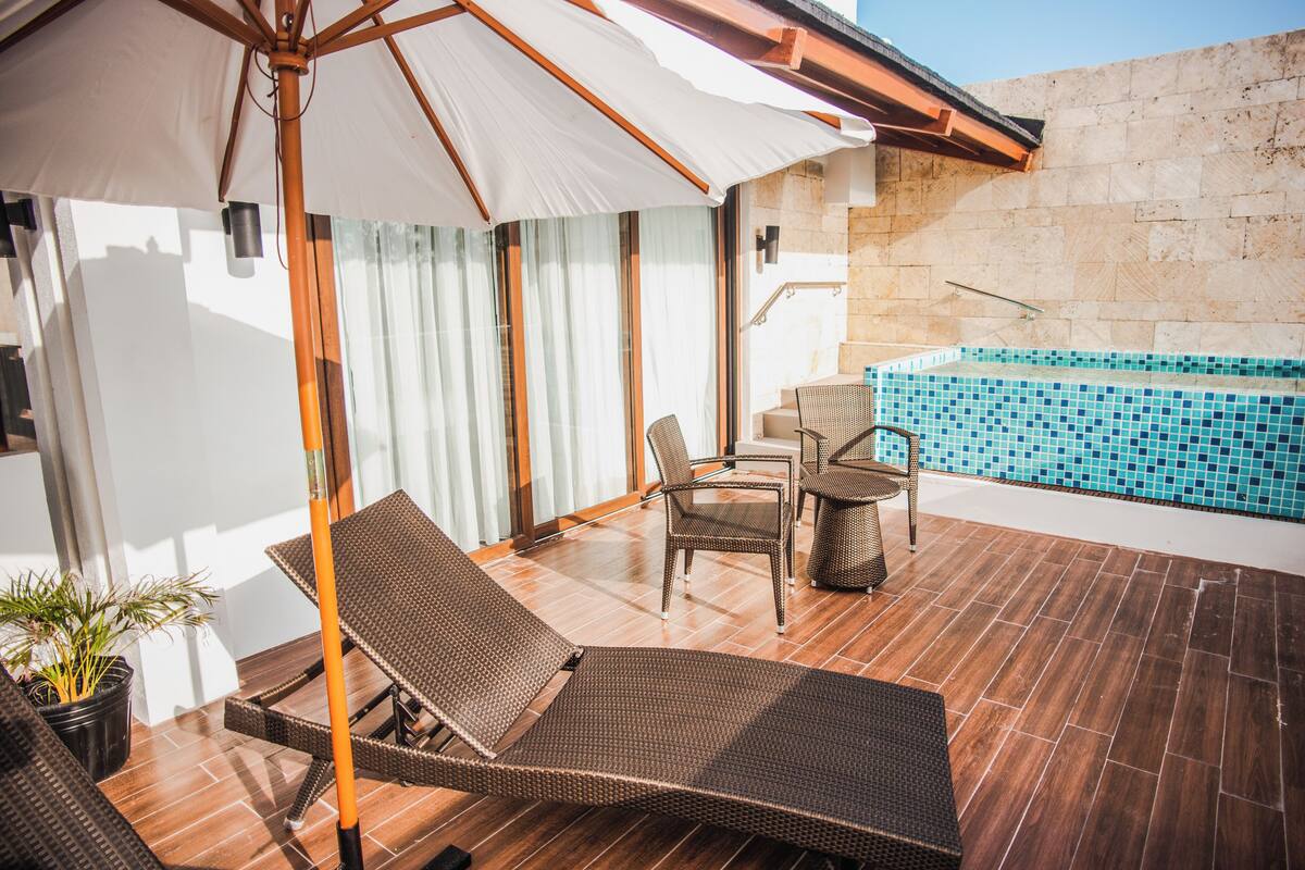 Un patio soleado con piscina, sillones de mimbre y una mesa.