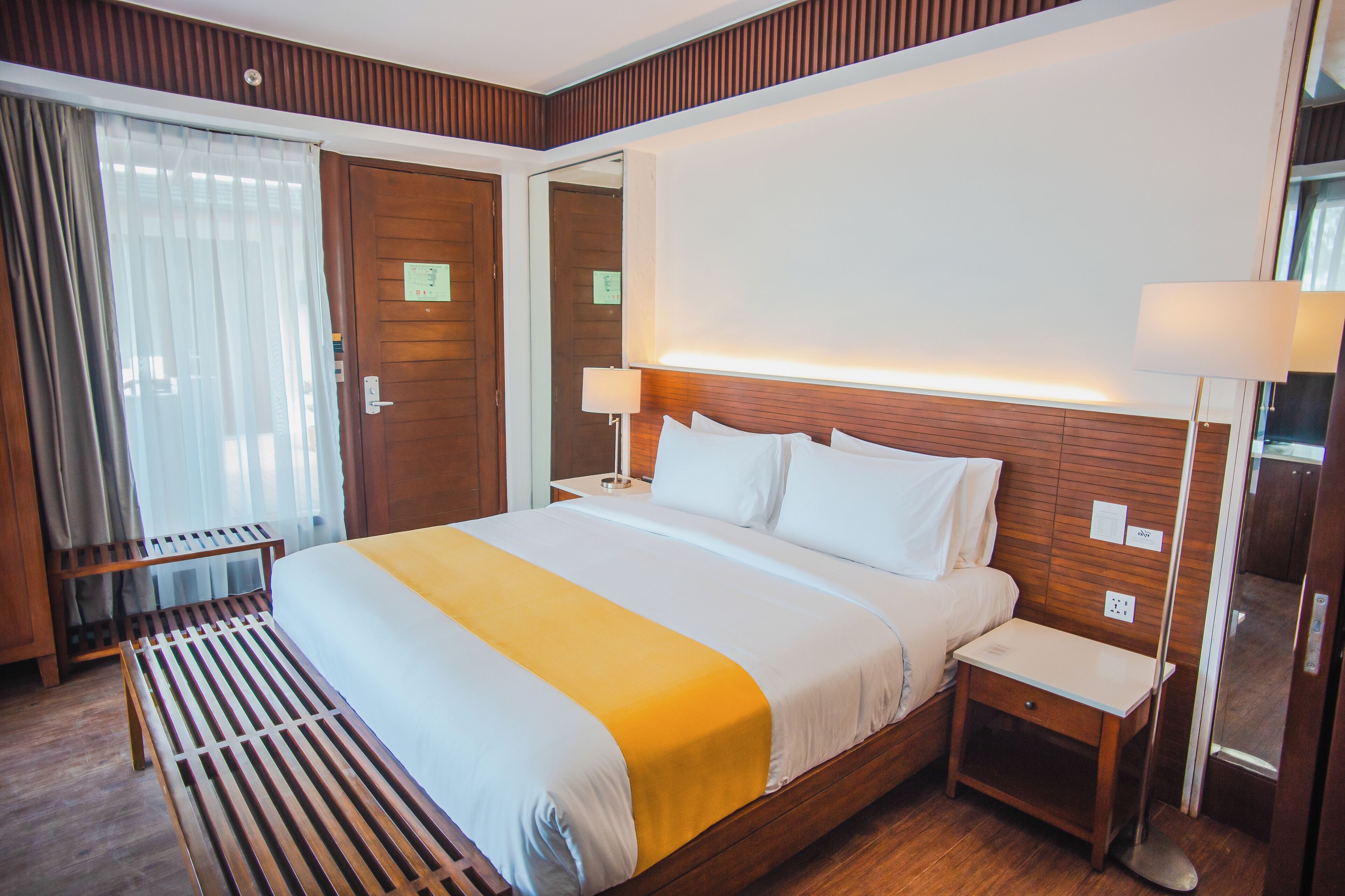 Een hotelkamer met een groot bed, nachtkastjes, een bankje en een spiegel.