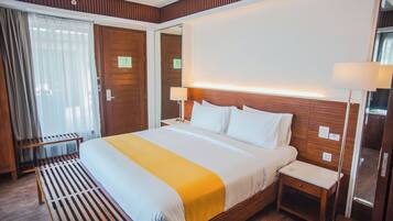 Een hotelkamer met een groot bed, nachtkastjes, een bankje en een spiegel.