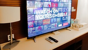 A television displaying a streaming service interface with a "Watch on Your Schedule" message, remote controls, and a white coffee table with a water bottle and mug. - Mandarin White Sand Boracay (Boracay Island)
