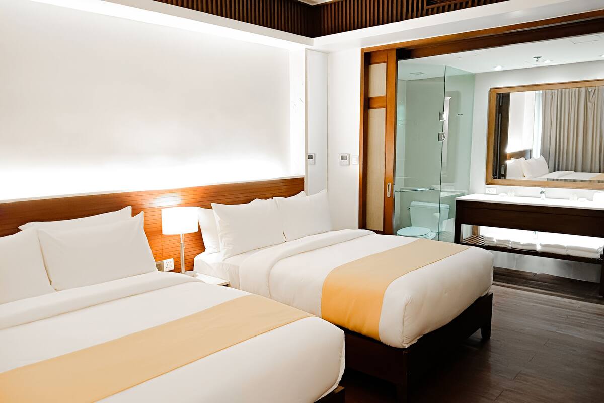 Habitación de hotel con dos camas, un cabecero de madera, una cabina de ducha de vidrio y un espejo grande.