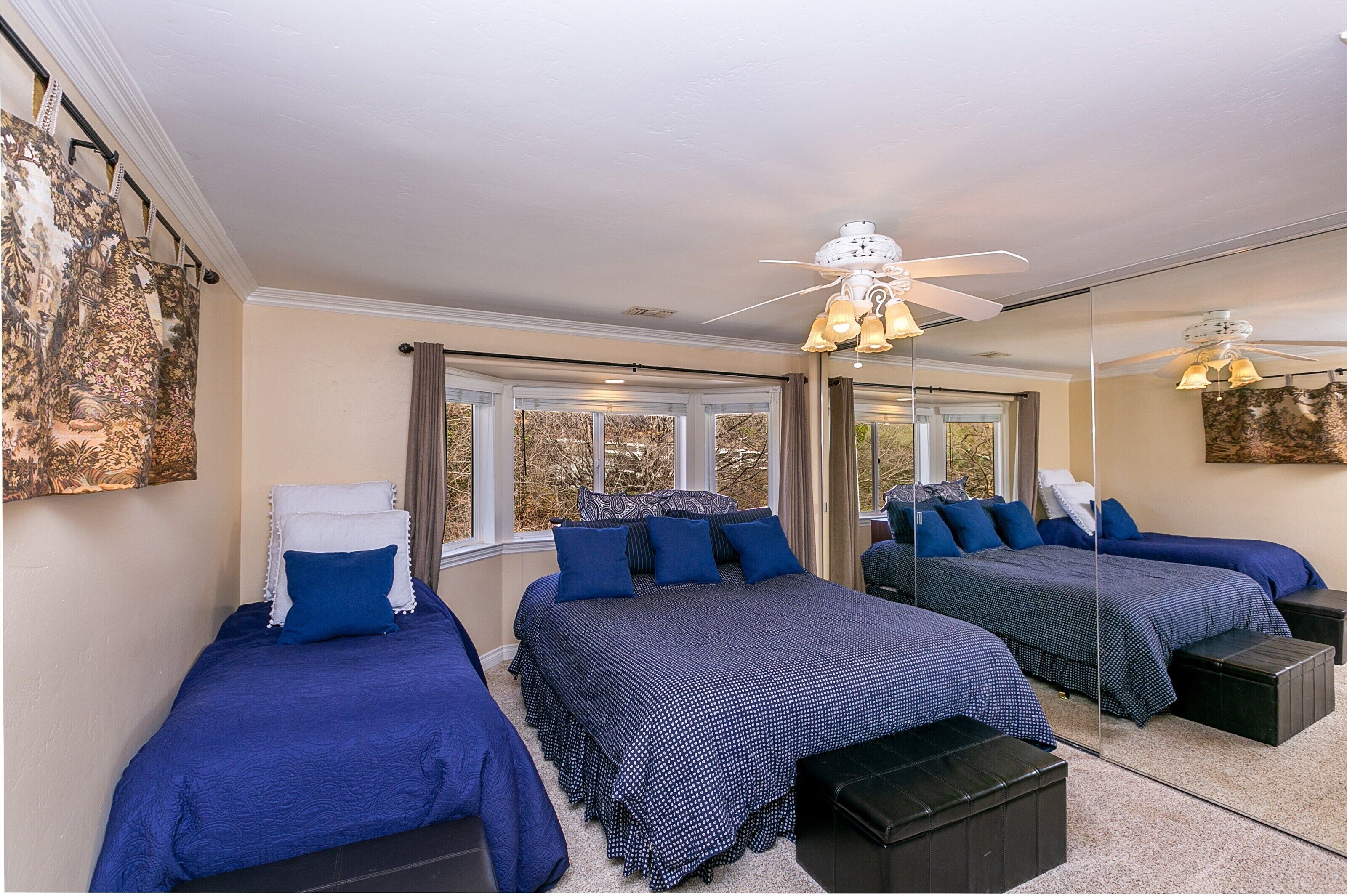 A bedroom with three beds, large windows, and a ceiling fan.