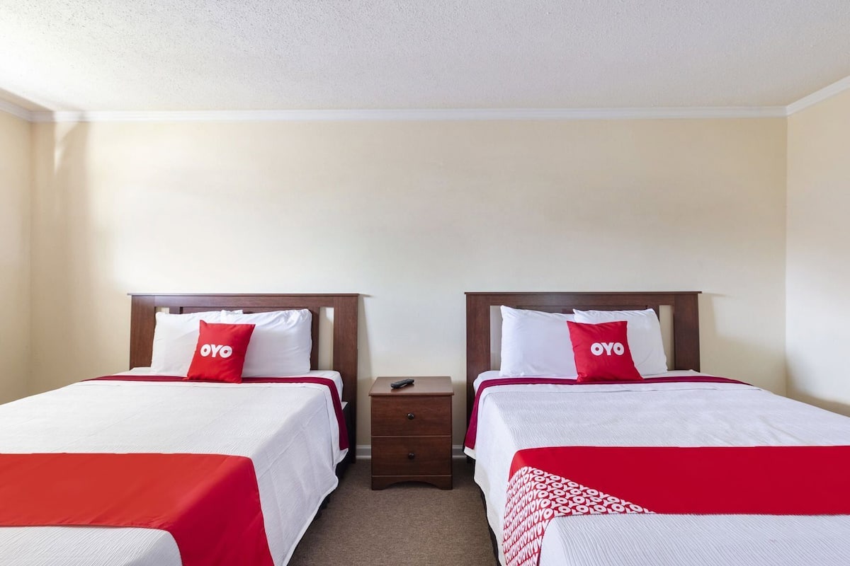 A hotel room with two beds, each with a red and white bedspread, a wooden headboard, and a nightstand with a remote control.