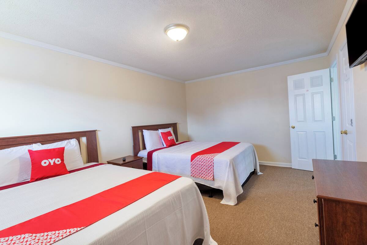 A hotel room with two beds, a TV, a wooden dresser, and a white door.