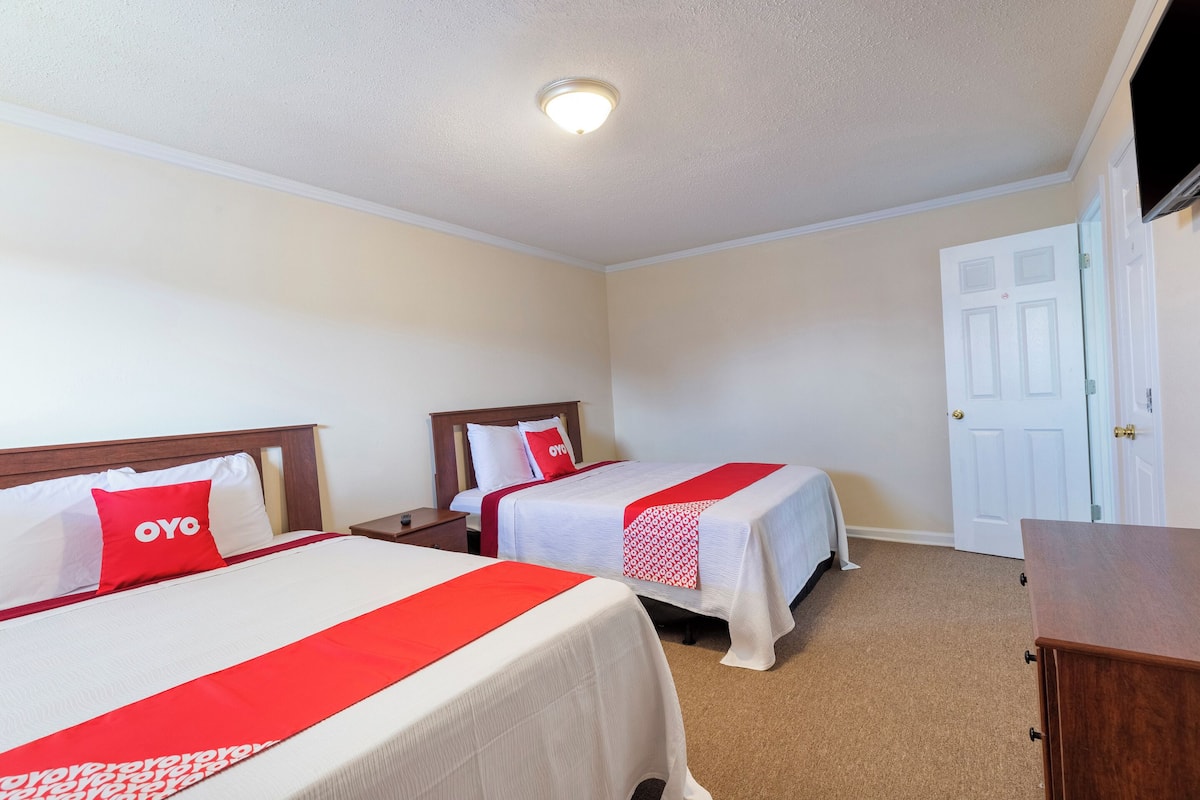 A hotel room with two beds, a TV, a wooden dresser, and a white door.