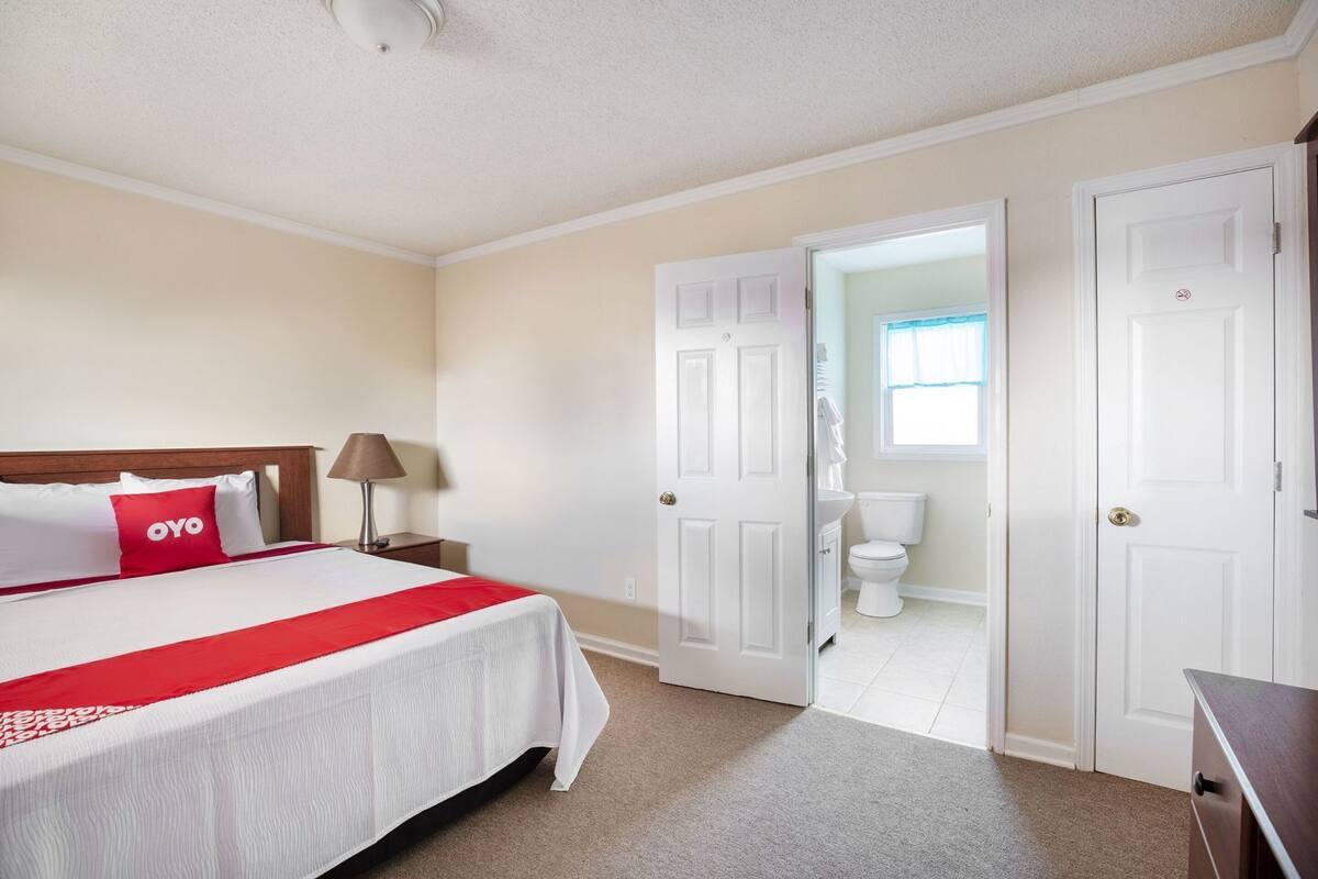A hotel room with a bed, a nightstand, a lamp, and a bathroom visible through an open door.