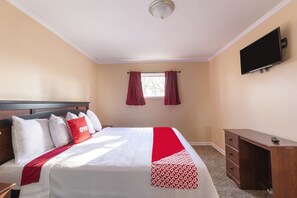 A hotel room with a bed, a desk, a TV, and a window with curtains.