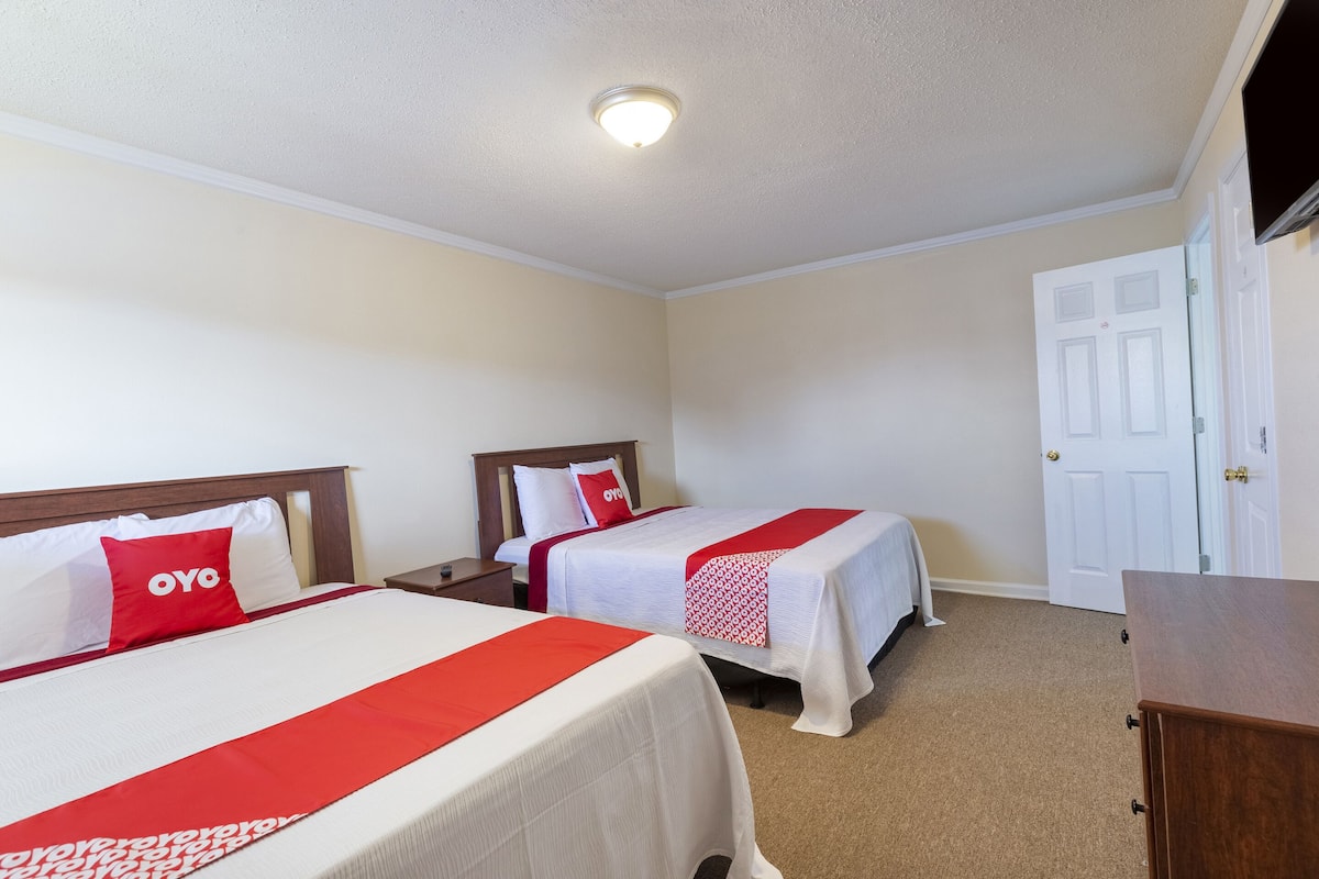 A hotel room with two beds, a TV, a wooden dresser, and a white door.