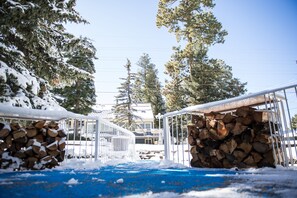 A snow-covered pathway leading to a building with stacked firewood on either side.