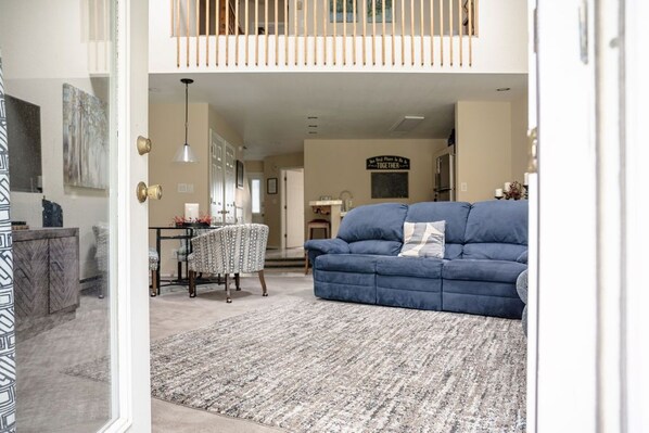 A spacious living room with a blue sofa, a patterned rug, and a dining area with a table and chairs.