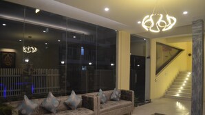 A modern living room with a sofa, a glass partition, and a staircase. - Ashira Inn (Greater Noida)