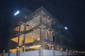 A modern multi-story building with large windows and a well-lit facade at night. - Ashira Inn (Greater Noida)