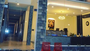 A hotel lobby with a reception desk, two red chairs, and a large window overlooking the street. - Ashira Inn (Greater Noida)