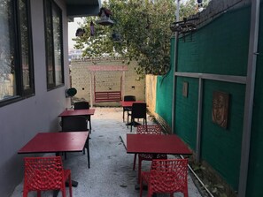 An outdoor seating area with tables and chairs, a brick wall, and a green fence. - Ashira Inn (Greater Noida)