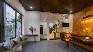 Un interior espacioso con un banco de madera, una mesa con un florero y una escalera que conduce a un nivel superior.