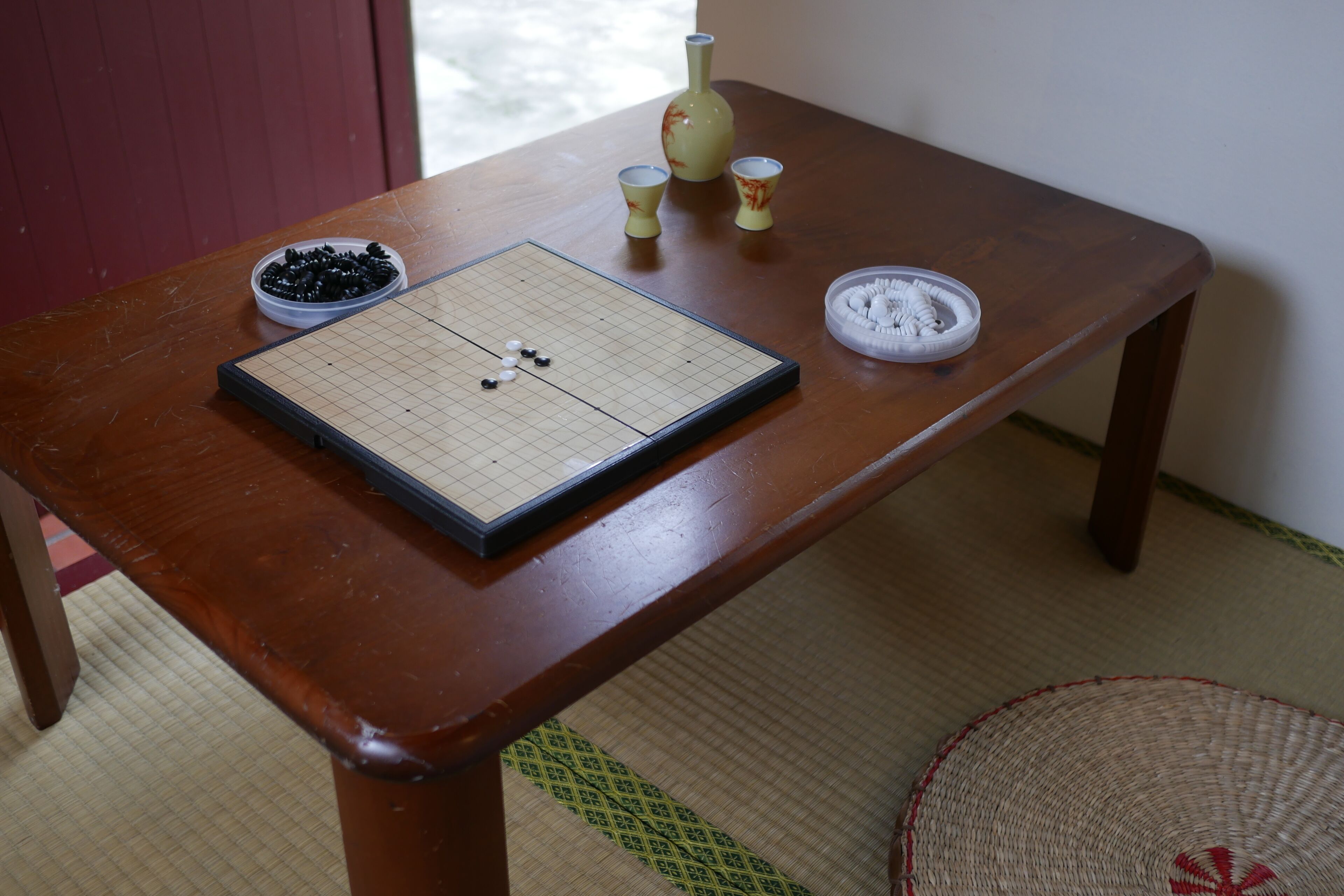 A wooden table with a Go board, a bowl of black beans, and a vase.