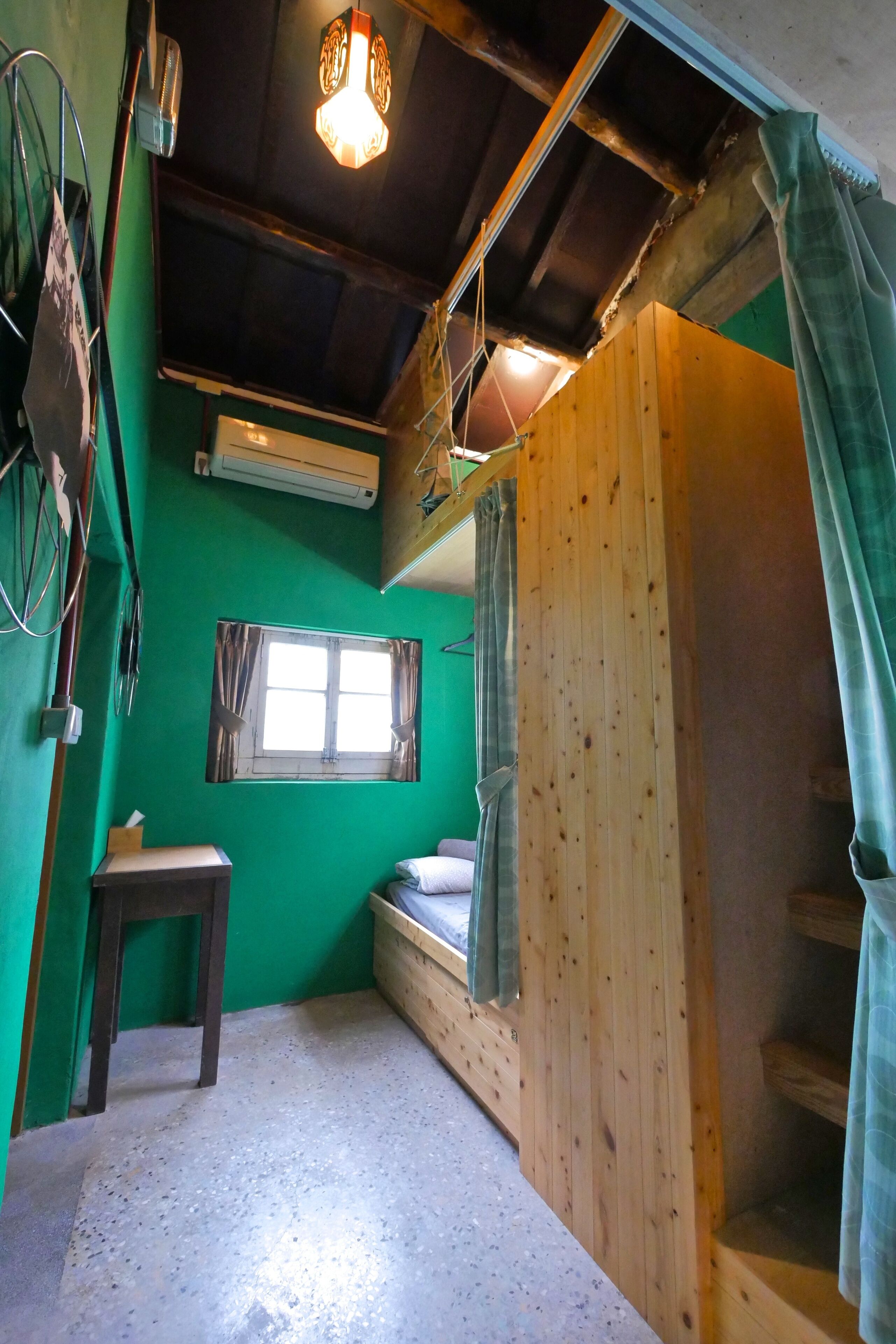 A small, cozy room with a green wall, a wooden bench, a small table, and a window.