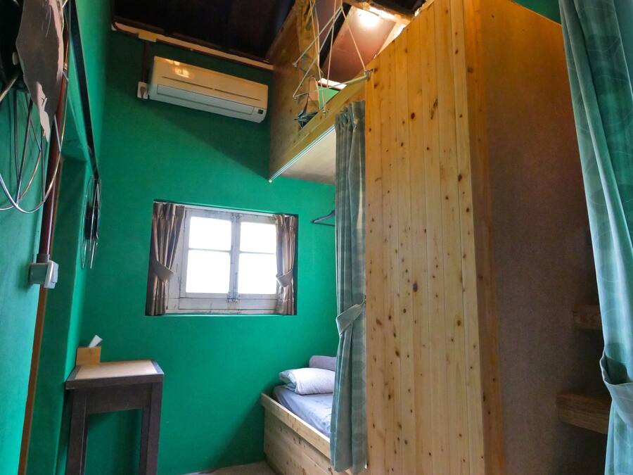A small, cozy room with a green wall, a wooden bench, a small table, and a window.